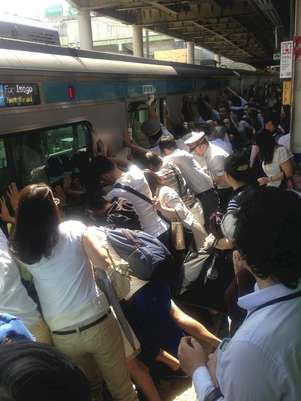 Imagem mostra os passageiros empurrando o vagão para salvar a mulher que caiu no vão Foto: orihiro Shigeta/Yomiuri Shimbun / AP
